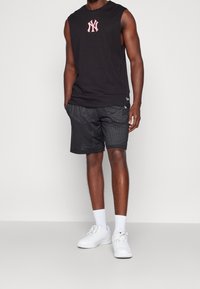 Black sleeveless tank top with white NY logo, paired with black mesh shorts featuring a textured pattern, complemented by white sneakers.