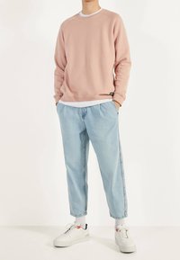 Sudadera rosa claro con cuello redondo y mangas largas, combinada con vaqueros azul claro de corte estrecho. Se lleva con zapatillas blancas, con detalles en rojo.