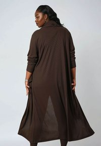 Brown ribbed long coat with a high collar, open back, and full sleeves. The fabric appears soft and flowing, with a relaxed silhouette.