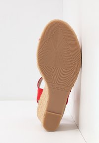 Semelle d'une sandale compensée rouge avec une semelle en caoutchouc texturée, nom de la marque "Tamaris" et taille 37 embossés sur la zone du talon.