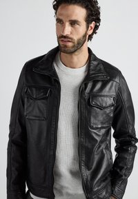 Zwart leren jack met een ritssluiting aan de voorkant, drukknopkraag en twee borstzakken. Heeft een gladde textuur en een aansluitend ontwerp.