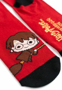 Calze rosse di cotone con un personaggio dei cartoni animati che indossa occhiali e tiene una bacchetta, con la punta nera e il testo "Harry Potter" in giallo.