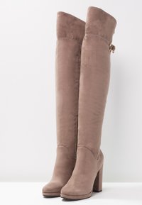 Botas de ante color topo hasta la rodilla, con un tacón grueso, detalles de costura sutiles y una hebilla decorativa en el lateral.