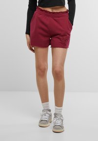 Bordeaux bomullsshorts med elastisk linning, frynset kant og broderte detaljer. Kombinert med grå sneakers og hvite ankelstrømper.