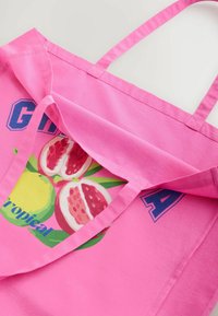 Borsa tote in cotone rosa con una grafica colorata di frutta, tra cui limone e melograno, con testo in grassetto e manici rinforzati.