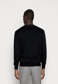 Zwarte sweatshirt met ronde hals, ribgebreide boorden en onderrand, gemaakt van een gladde stof, met een subtiele patch op de achterkant.