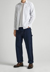Camisa de algodón a rayas, blanca y azul; camiseta gris debajo; pantalones tipo cargo azul oscuro; botas marrones con cordones.
