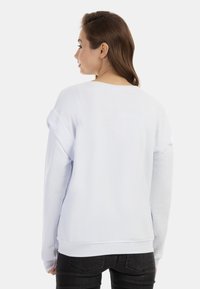 Bílý oversized svetr s dlouhými rukávy, žebrovanými manžetami a lemem. Měkká textilie s kulatým výstřihem. Černé džíny doplňují outfit.