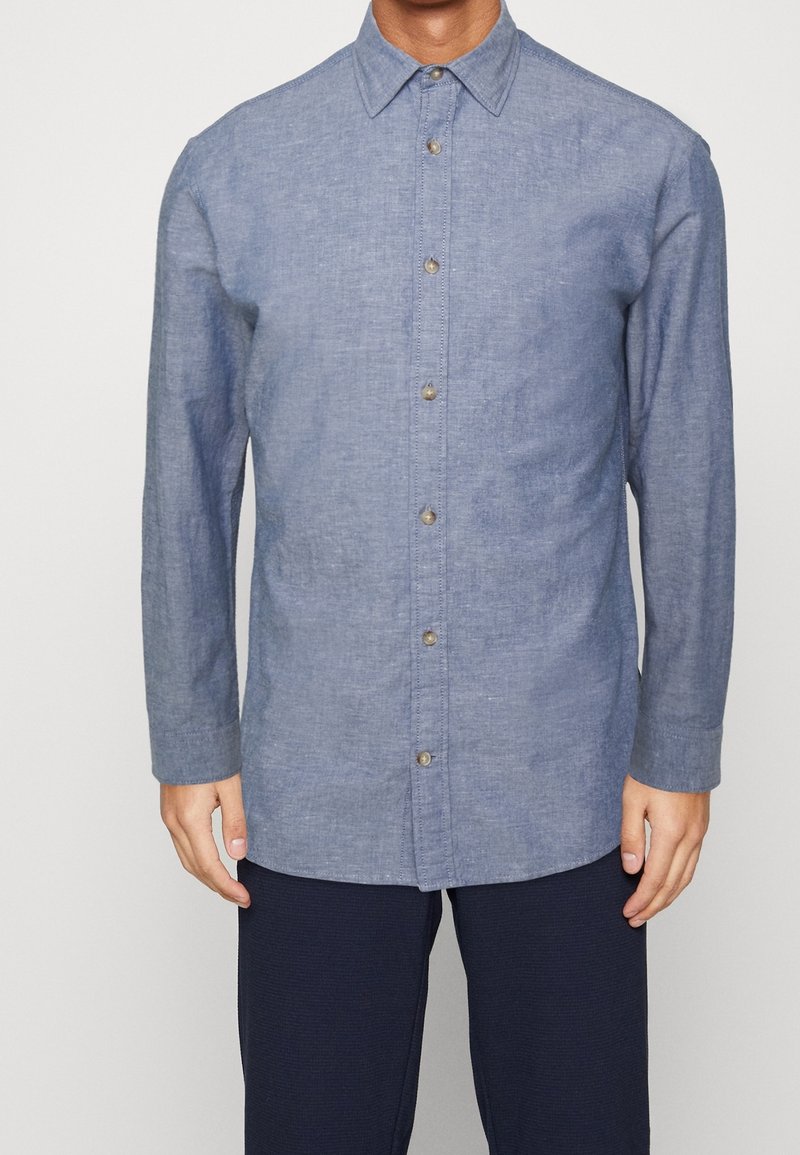 Jasnoniebieska, długouvieczorna koszula zapinana na guziki, wykonana z teksturowanej tkaniny, z charakterystycznym kołnierzykiem i widocznymi guzikami z przodu.