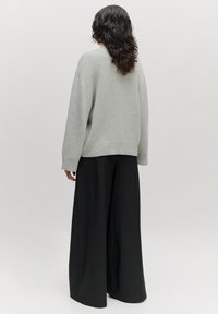 Hellgrauer, übergroßer Pullover mit geripptem Saum und Bündchen, kombiniert mit lockeren, weit geschnittenen schwarzen Hosen. Einfaches und minimalistisches Design.