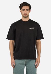 Sort bomulds t-shirt med rund halsudskæring og korte ærmer. Har et lille hvidt broderet logo på venstre bryst.