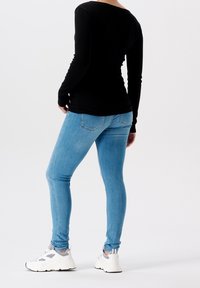 Musta pitkähihainen paita, vaaleansiniset skinny-farkut ja valkoiset lenkkarit harmailla yksityiskohdilla. Kirkas tausta, keskittyminen asusteeseen.