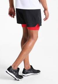 Svarta sportshorts med röd underlayer, designade för rörelse; parat med svarta och vita löparskor med övre i mesh.
