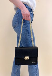 Borsa a tracolla in pelle nera con catena dorata, forma rettangolare e chiusura frontale. Presenta un logo sottile nell'angolo in basso a destra.