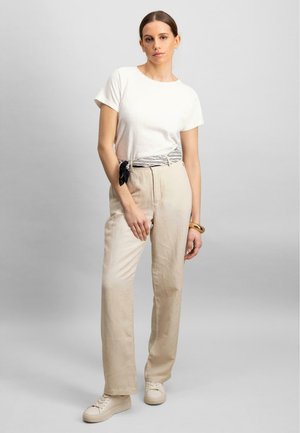 Creme t-shirt med korte ærmer, parret med lysebeige linnedbukser, fremhævet af et sort-hvid stribet bælte og hvide sneakers.