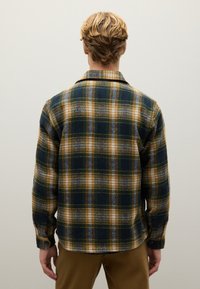 Flanellen overhemd in een gele, groene en blauwe ruitpatroon. Heeft een kraag en knoopsluitingen bij de manchetten. Zachte textuur, relaxte pasvorm.