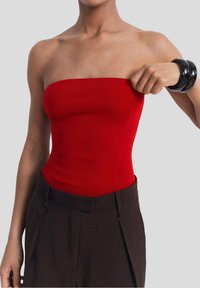 Röd ribbad bandeau-top med en figurnära design, matchad med högmidjade mörkbruna byxor. Modellen justerar toppen.