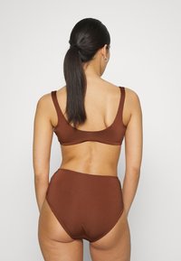 Conjunto de biquíni castanho com um topo ajustado de alças largas e parte de baixo de cintura alta, ambos em tecido liso. Sem padrões ou detalhes visíveis.