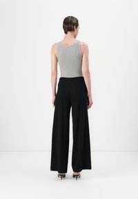 Canotta grigia a coste abbinata a pantaloni neri a gamba larga, che mettono in evidenza una texture liscia e una silhouette pulita. Vista posteriore con accessori minimi.