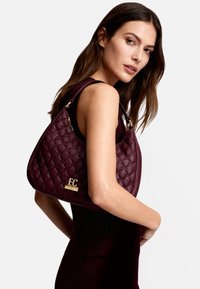 Borsa trapuntata color bordeaux con dettagli in metallo dorato e logo. Materiale morbido e liscio, con silhouette curva e tracolla.
