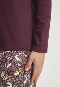 Bordeaux lange mouwen top met een soepele textuur, gecombineerd met gestreepte broeken met bloemen en dieren in paarse, gele en groene tinten.