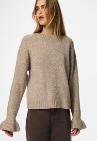 Beige kötött pulóver bordás textúrával, széles, harang alakú ujjal és kerek nyakkivágással. Sötétbarna nadrággal párosítva.