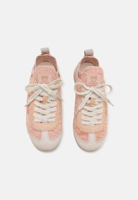 Gaiši rozā sporta apavi ar teksturētu adītu virsu, baltajām auklām un krēmkrāsas purngaliem. Uzmundrina logo uz mēles un aizmugurējā cilpa.