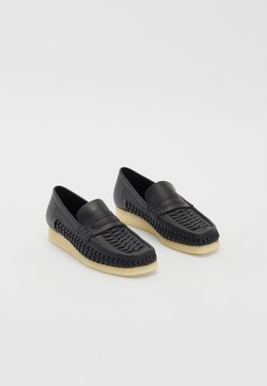 Mocassini in pelle nera con dettagli intrecciati, punta arrotondata e suola chiara e strutturata. Finitura liscia con design a profilo basso.