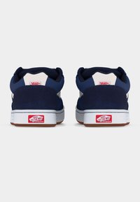 Σκούρα μπλε αθλητικά Vans, εμφανιζόμενα από πίσω, με λευκή μεσαία σόλα και κόκκινα λογότυπα «Off The Wall» στη φτέρνα και στην πίσω ταμπέλα πάνω.