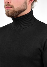 Schwarzer Rollkragenpullover aus geripptem Strickstoff, mit hohem Kragen und tailliertem Schnitt. Weiche Textur ohne sichtbare Muster.