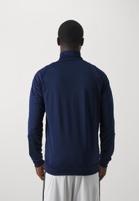 Marineblå hettejakke med høyt krage og lange ermer. Laget av glatt stoff med en tettsittende design. Ingen synlige logoer eller mønstre.