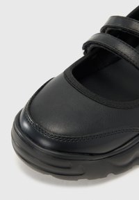 Zapato de cuero negro con punta redondeada, dos correas ajustables y una suela de goma texturizada con una ligera curvatura para mayor soporte.
