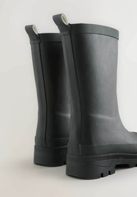 Bottes en caoutchouc noires avec une texture lisse, tige haute et bandes de grip texturées en haut et en bas. Dotées de semelles robustes pour une bonne adhérence.