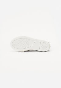 Bílá gumová podrážka boty s texturou a obdélníkovou vzorovou plochou na neutrálním pozadí.