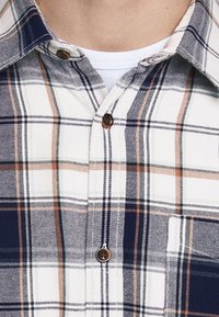 Geruite shirt in wit, marineblauw en oranje tinten. Knop-down kraag, bruine knopen en een borstzak. Katoenen stof met een zachte textuur.