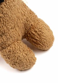 Weicher, beige Plüsch-Teddybärfuß mit einer strukturierten, lockigen Oberfläche und runder Form, die feine Details auf einem weißen Hintergrund zeigt.