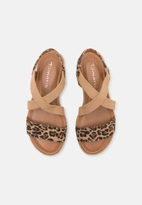Sandaler med leopardprint og et brunt elastisk krydsdesign, polstret sål og en struktureret ydersål. Farvepaletten indeholder tan og brun.
