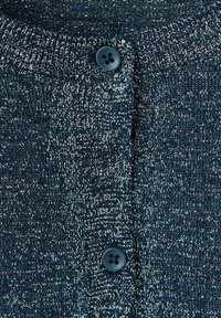 Mörkblå stickad tyg med metalliska silvertrådar, med två marinblå knappar och ribbat krage.