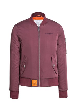 Burgundowa kurtka bombowca z zamkiem z przodu, dwiema bocznymi kieszeniami, ściągaczami u mankietów oraz jasnopomarańczową podszewką. Zawiera haft z logo.