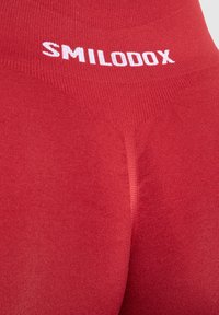 Leggings rossi con una texture liscia, vita alta che presenta il marchio bianco "SMILODOX" sulla parte superiore. Design aderente senza motivi degni di nota.