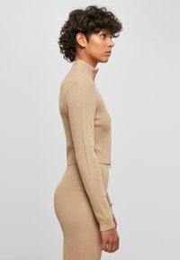 Beige ribbad tröja med hög krage och l�ånga ärmar, kort design, mjuk textur och åtsittande stil, bärs med matchande underdel.