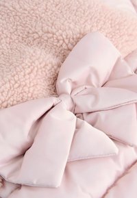Mjukt rosa filttäcke med plysch, texturerad fleece på ena sidan och slät satäng på den andra, prytt med en stor rosett.