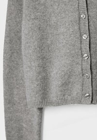 Cardigan en maille gris doux avec ourlet côtelé et six boutons argentés alignés verticalement le long de l’ouverture frontale.