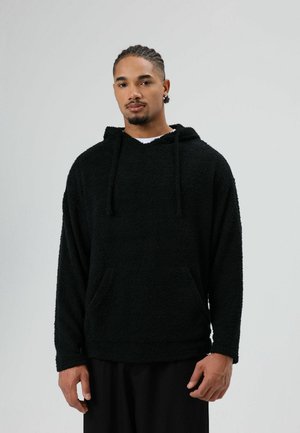 Zwarte fleece hoodie met een zachte textuur, voorzak en verstelbare capuchon met trekkoord. Oversized pasvorm en lange mouwen.