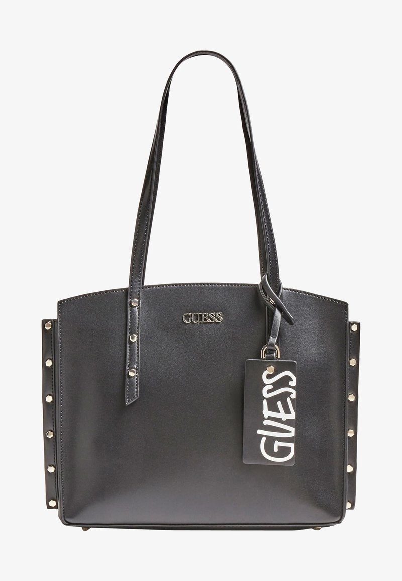 Sac cabas noir Guess avec longues anses, détails cloutés sur les côtés, logo en métal et étiquette de marque rectangulaire attachée.