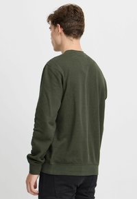 M�ørkegrøn sweatshirt i ribbet tekstur med rund hals, lange ærmer og en let tætsiddende silhuet. Ingen synlig branding eller mønstre.