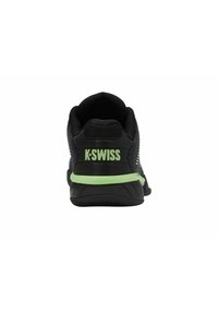 Chaussure de sport noire avec un dessus en maille et une bande d'accentuation verte, dotée d'une semelle texturée et du logo "K-Swiss" sur le talon.
