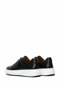 Zapatillas de cuero negras con una suela de goma blanca. Presentan una punta redondeada, detalles cosidos y un diseño de cordones. Textura suave en toda la superficie.