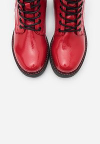 Botines de cuero rojo brillante, con cordones negros, puntera redondeada y costuras negras en contraste a lo largo de la suela. Superficie de textura suave.