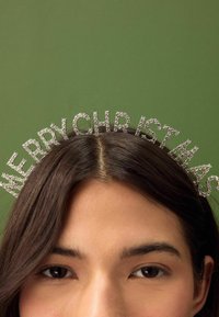 Sølv hårbånd med "GLÆDELIG JUL" i krystallater. Skinnende finish, sat mod en grøn baggrund.